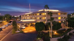 A multi-story hotel with a parking lot, a flagpole, and well-lit exterior.