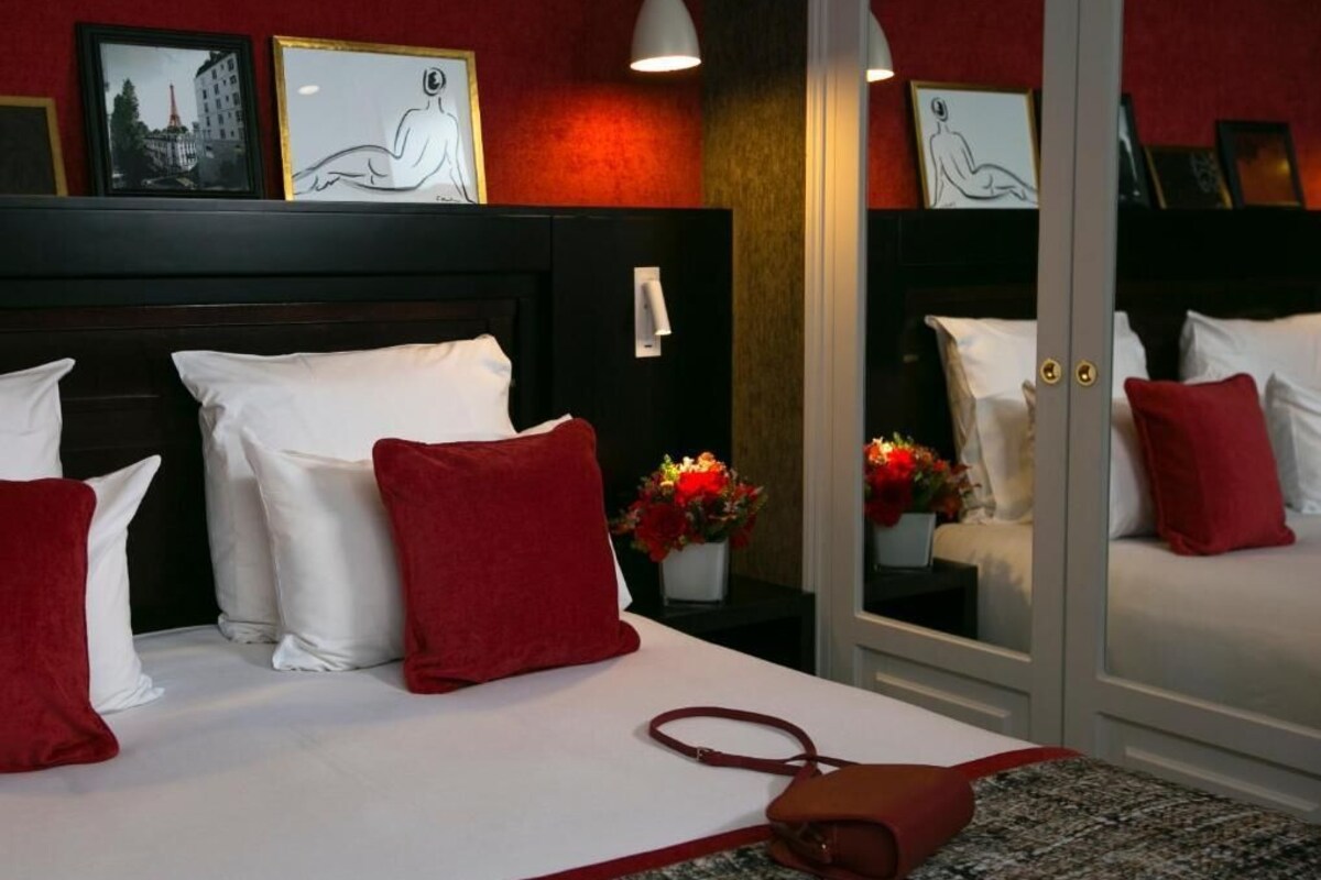 Una habitación de hotel con cama, almohadas, un bolso de mano y cuadros en la pared.
