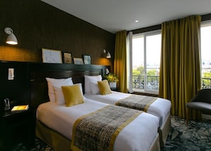 A hotel room with two beds, a nightstand, a chair, a window with curtains, and a balcony view. - Hôtel de Neuville (Paris)