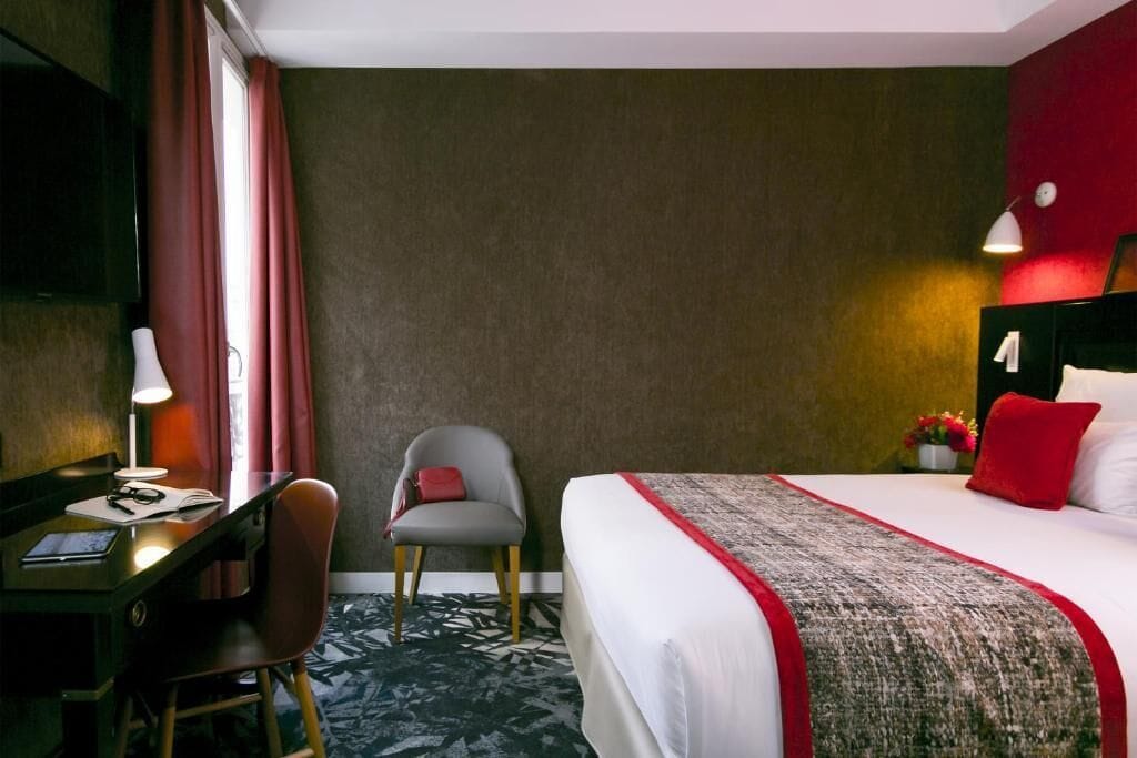 Een hotelkamer met een bed, bureau, stoel, lamp en een televisie.