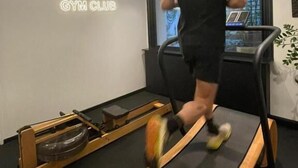 Una persona corre en una cinta de correr en un gimnasio con un letrero de neón que dice 'NEUVILLE GYM CLUB'.