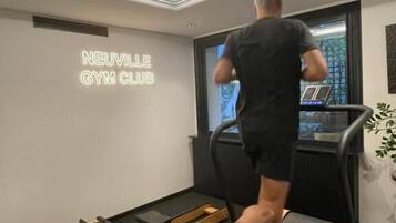 Une personne court sur un tapis de course dans une salle de sport, et un panneau au néon indique : « NEUVILLE GYM CLUB ».