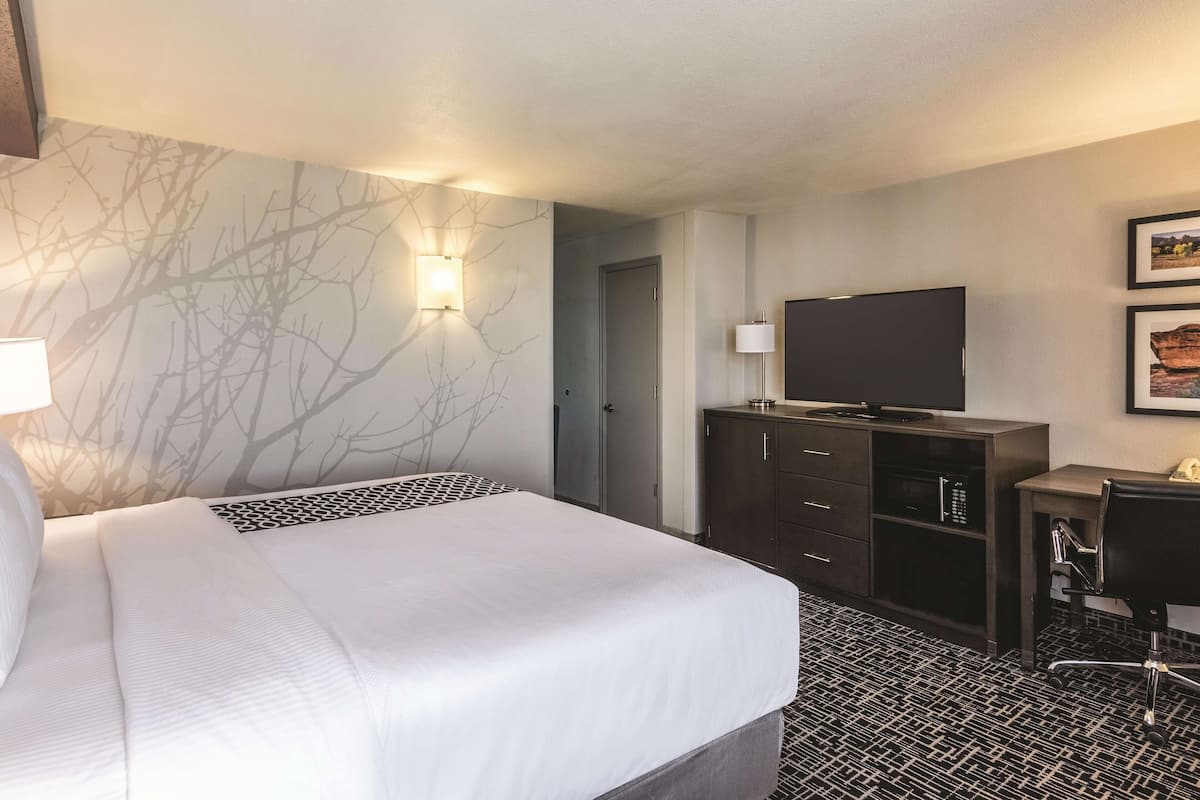 A hotel room with a bed, a desk, a television, and a wall-mounted light.