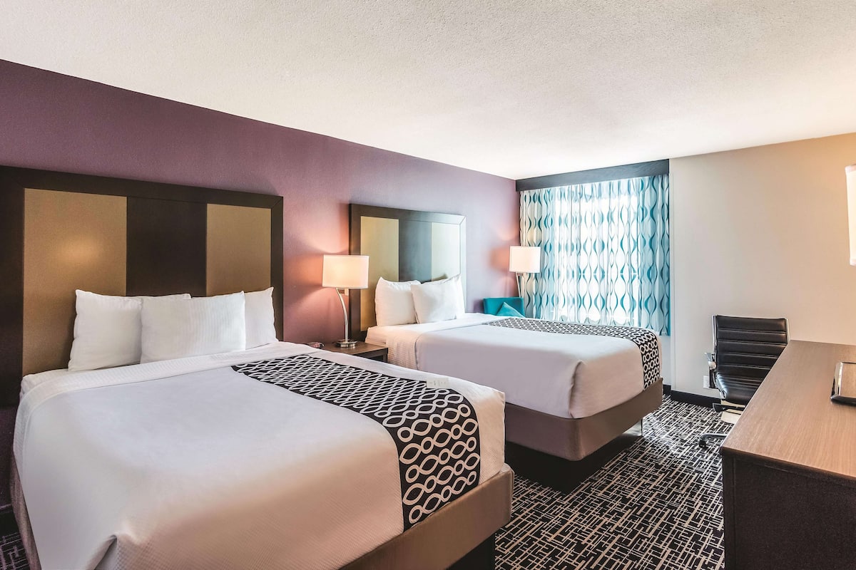 A hotel room with two beds, a desk, and a chair.