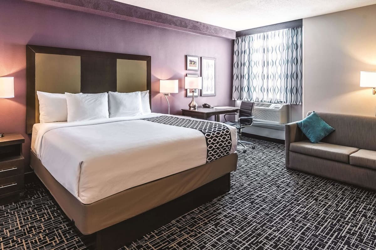 A hotel room with a large bed, a desk, a chair, a sofa, and a patterned carpet.