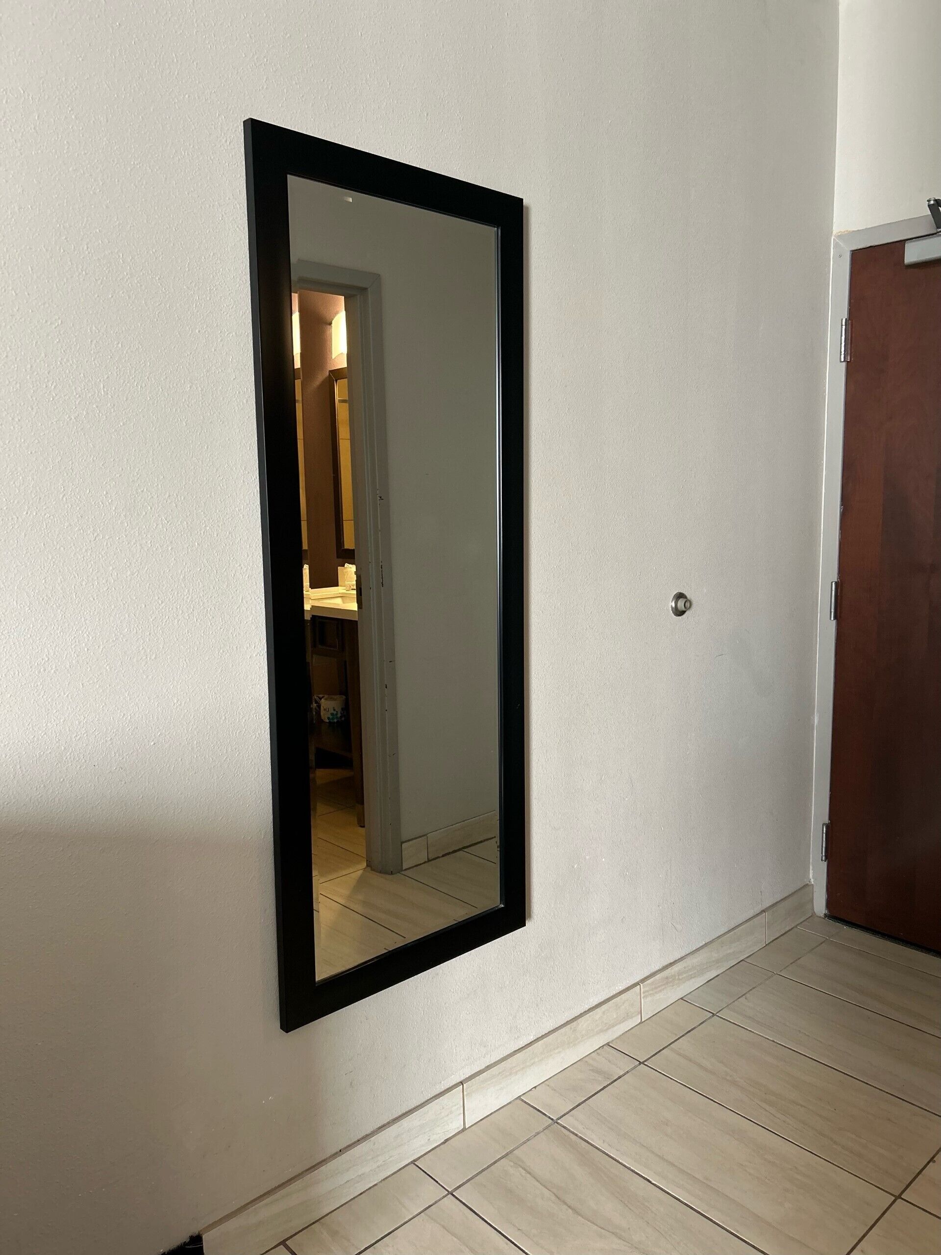 A hallway with a large mirror on the wall, a wooden door, and a tiled floor.