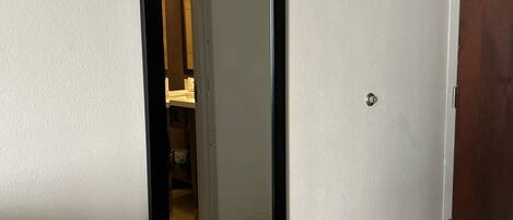 A hallway with a large mirror on the wall, a wooden door, and a tiled floor.