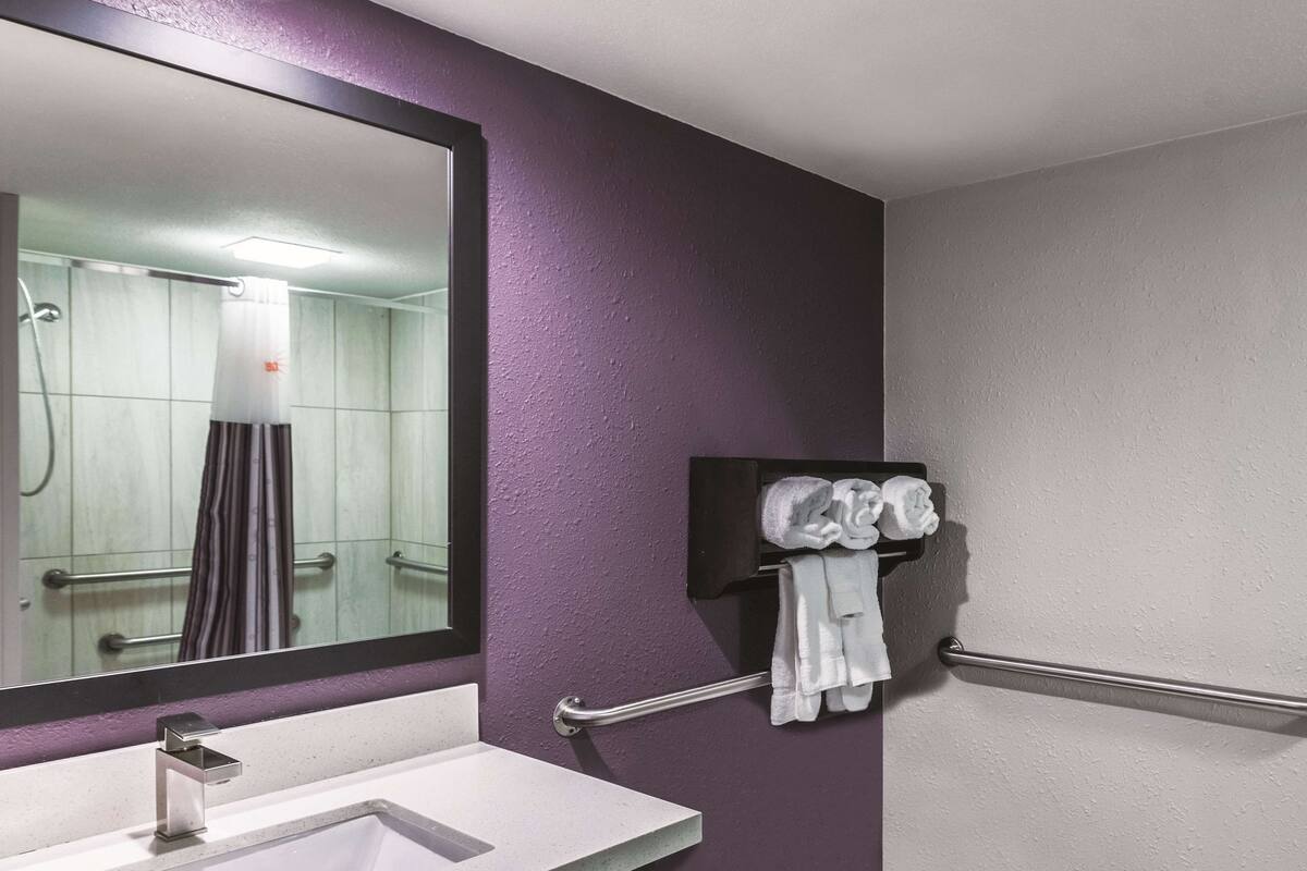A bathroom with a white sink, a mirror, a towel rack with towels, and a shower area.