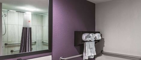 A bathroom with a white sink, a mirror, a towel rack with towels, and a shower area.