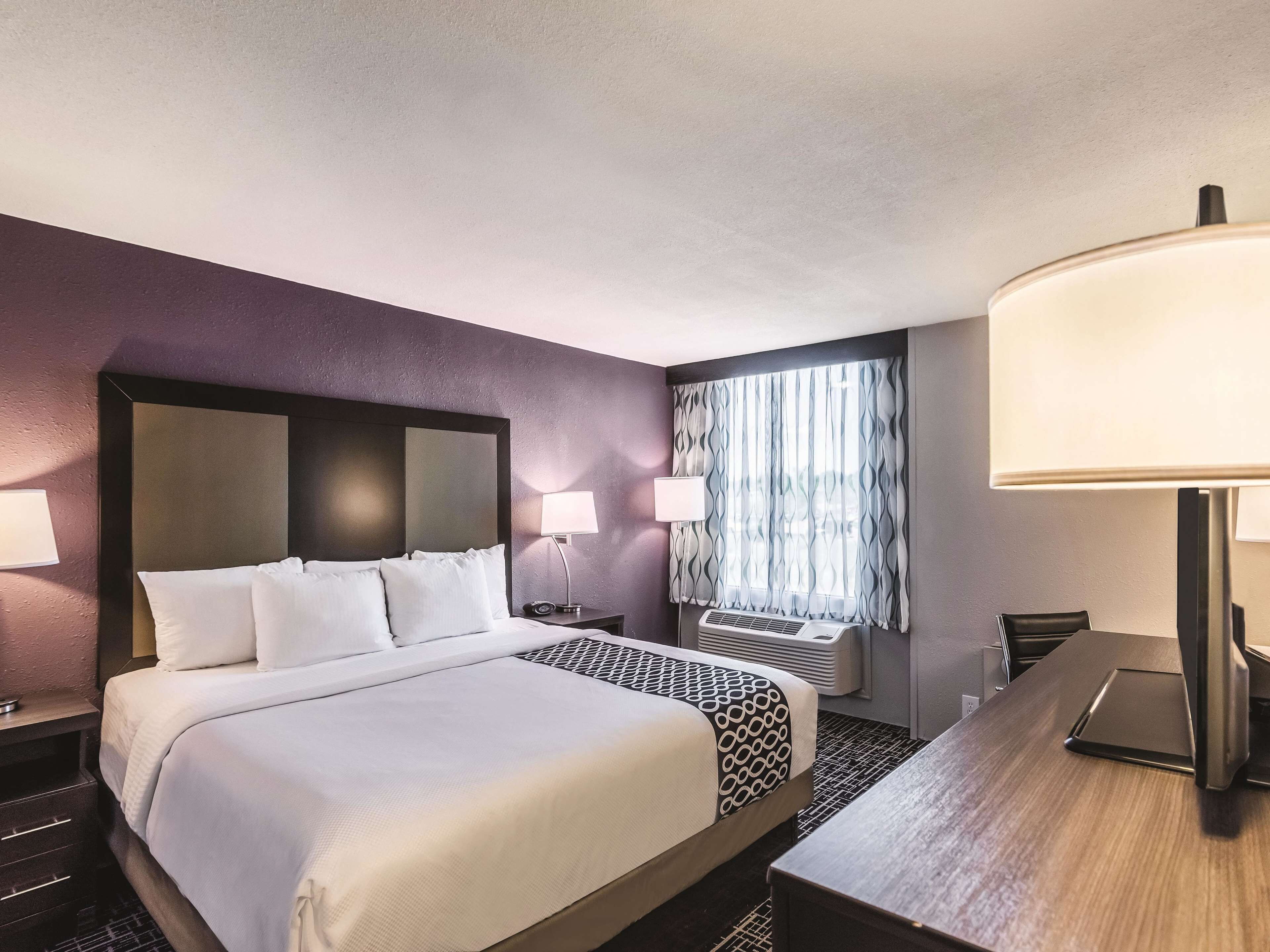 Une chambre d’hôtel avec un grand lit, deux lampes de chevet, un bureau, une chaise et une fenêtre avec des rideaux.