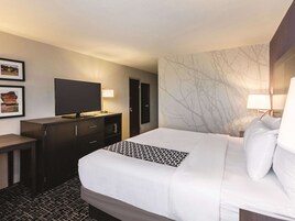 Habitación de hotel con una cama grande, un televisor en una cómoda, un escritorio y una pared con un diseño de árbol.