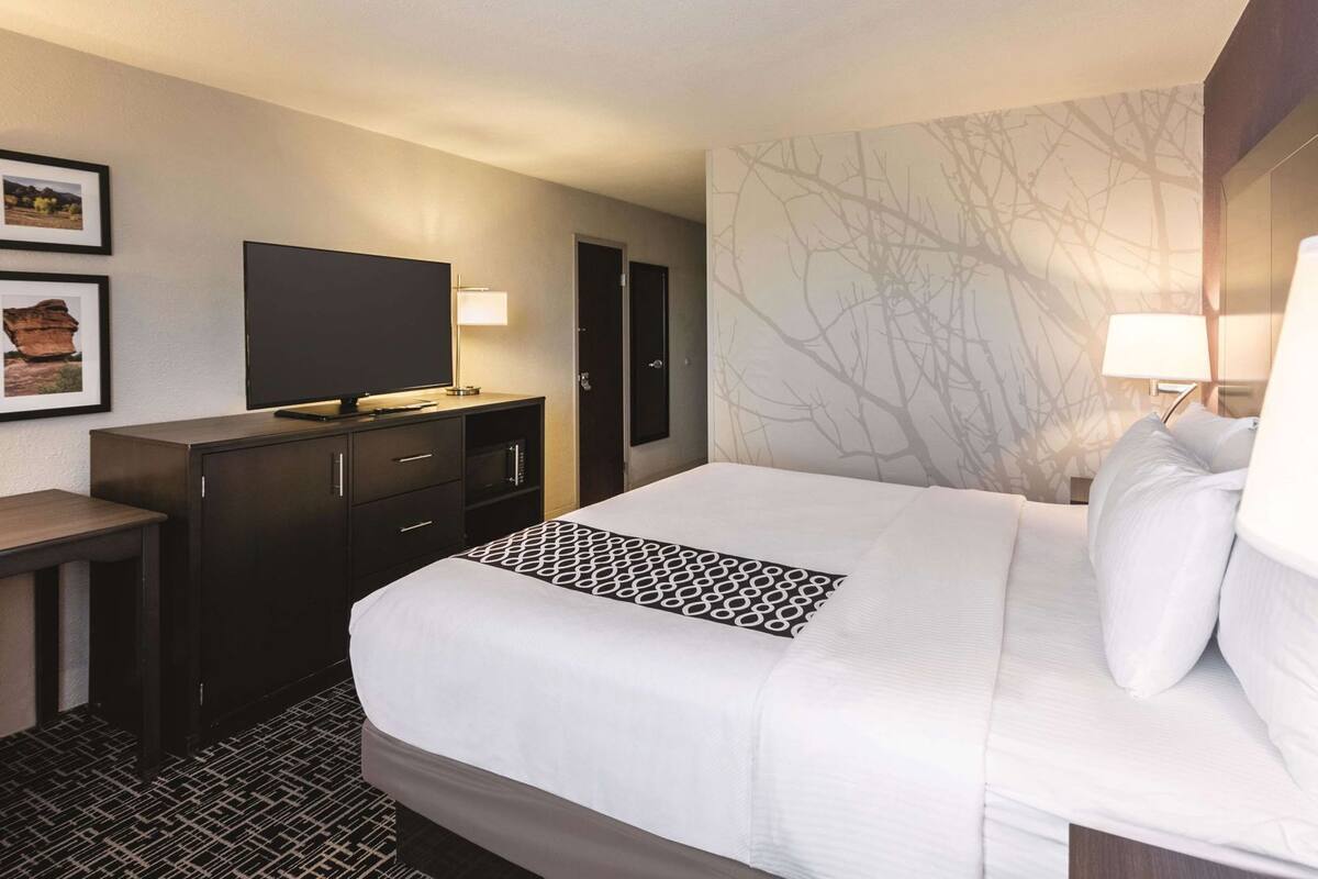 A hotel room with a bed, a TV, a desk, and a dresser.