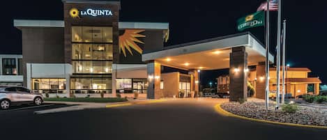 Hotel La Quinta de noche con una entrada bien iluminada, un gran logo de sol y banderas.