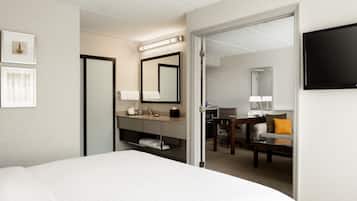 Een hotelkamer met een bed, een badkamer met een wastafel en spiegel, een bureau met stoel, en een televisie aan de muur.
