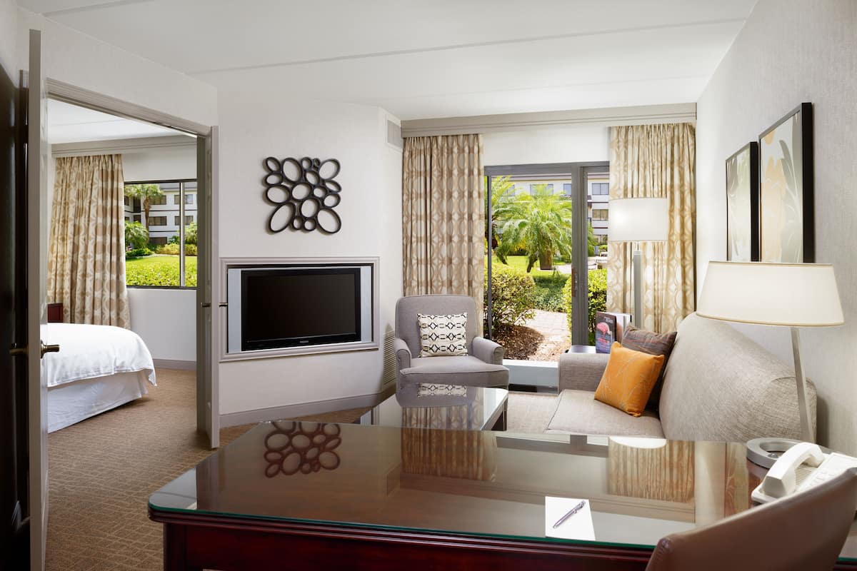 Habitación de hotel con cama, televisor, sofá, mesa de centro y vistas al exterior.