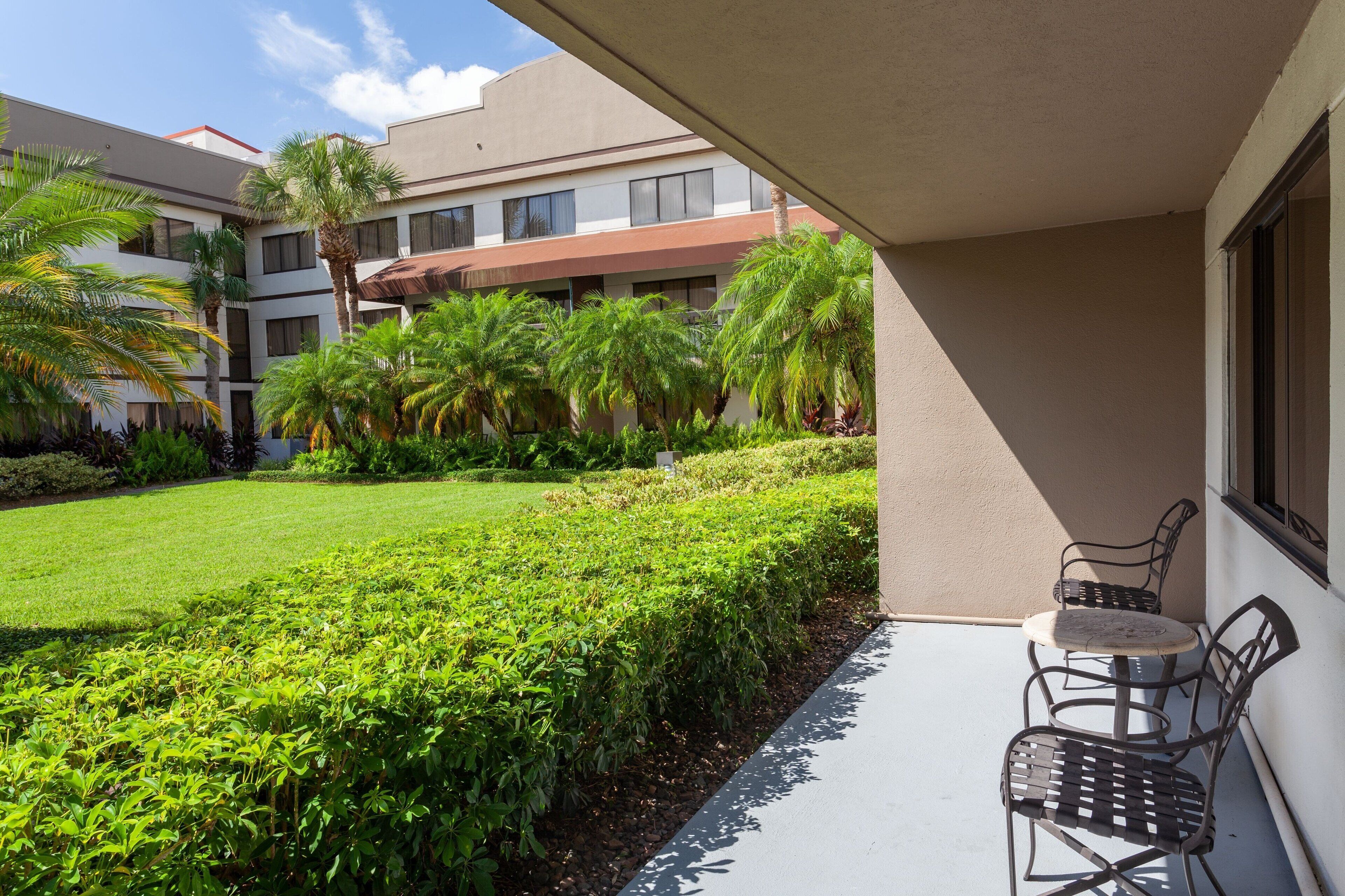 A courtyard with a small seating area, palm trees, and a building with multiple windows.