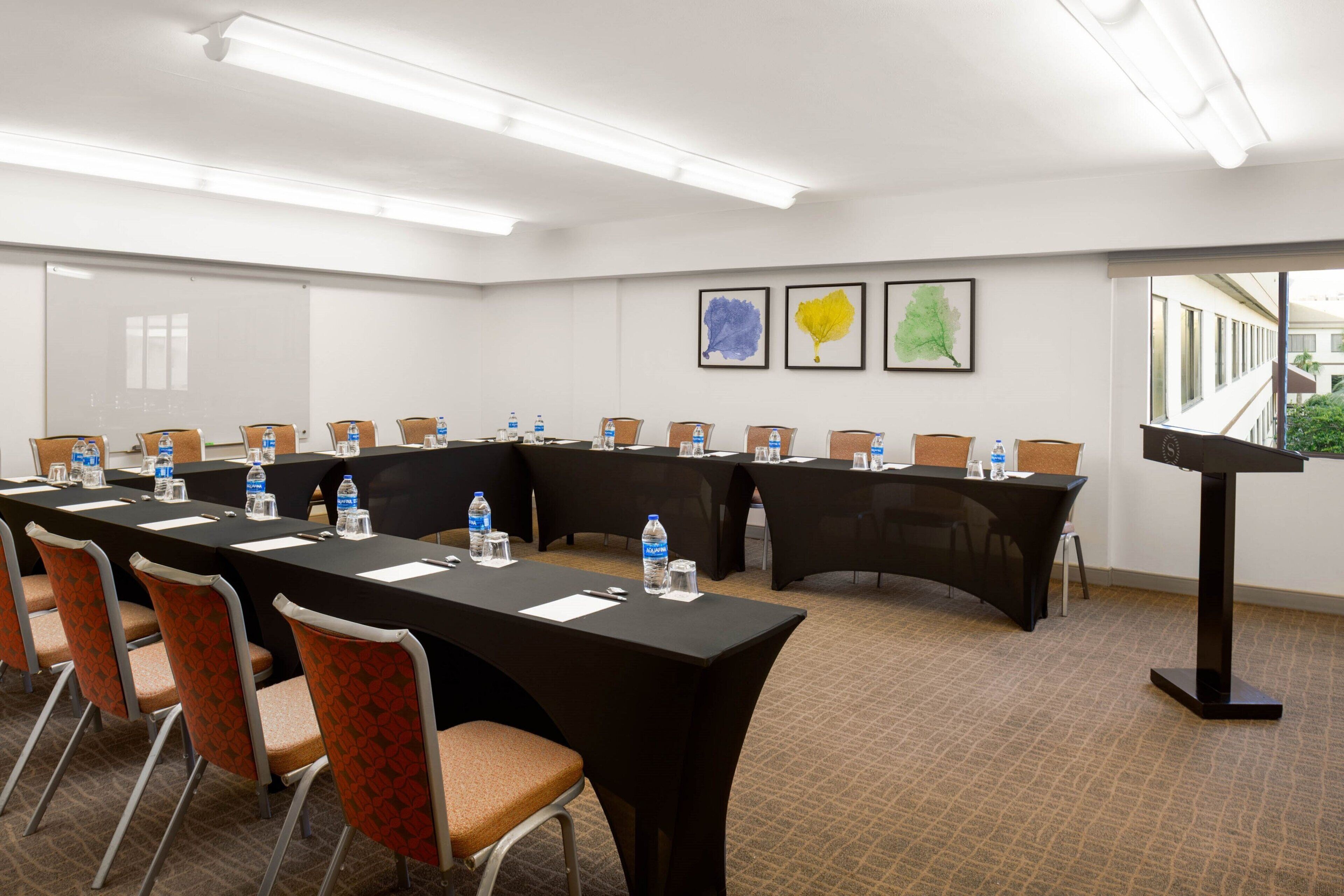 A conference room with long tables, chairs, water bottles, and a podium.