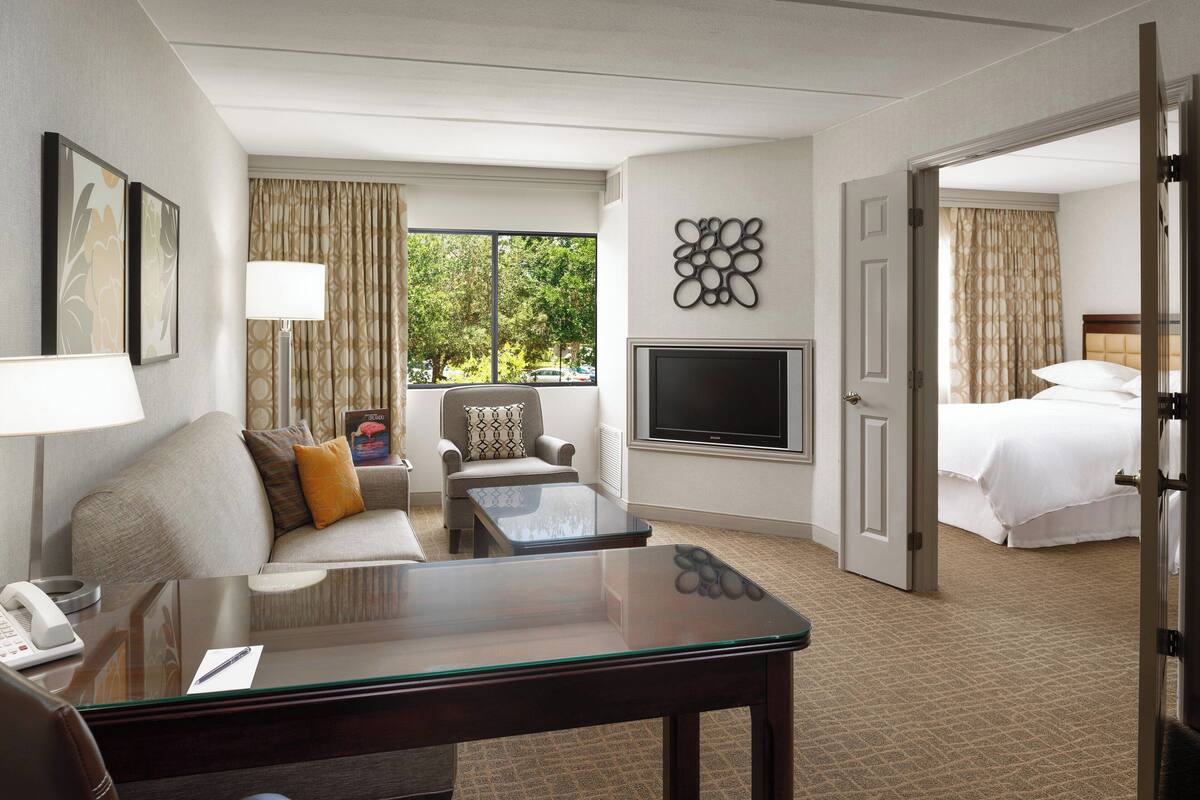 Habitación de hotel con sofá, sillón, mesa de centro, televisión y cama.
