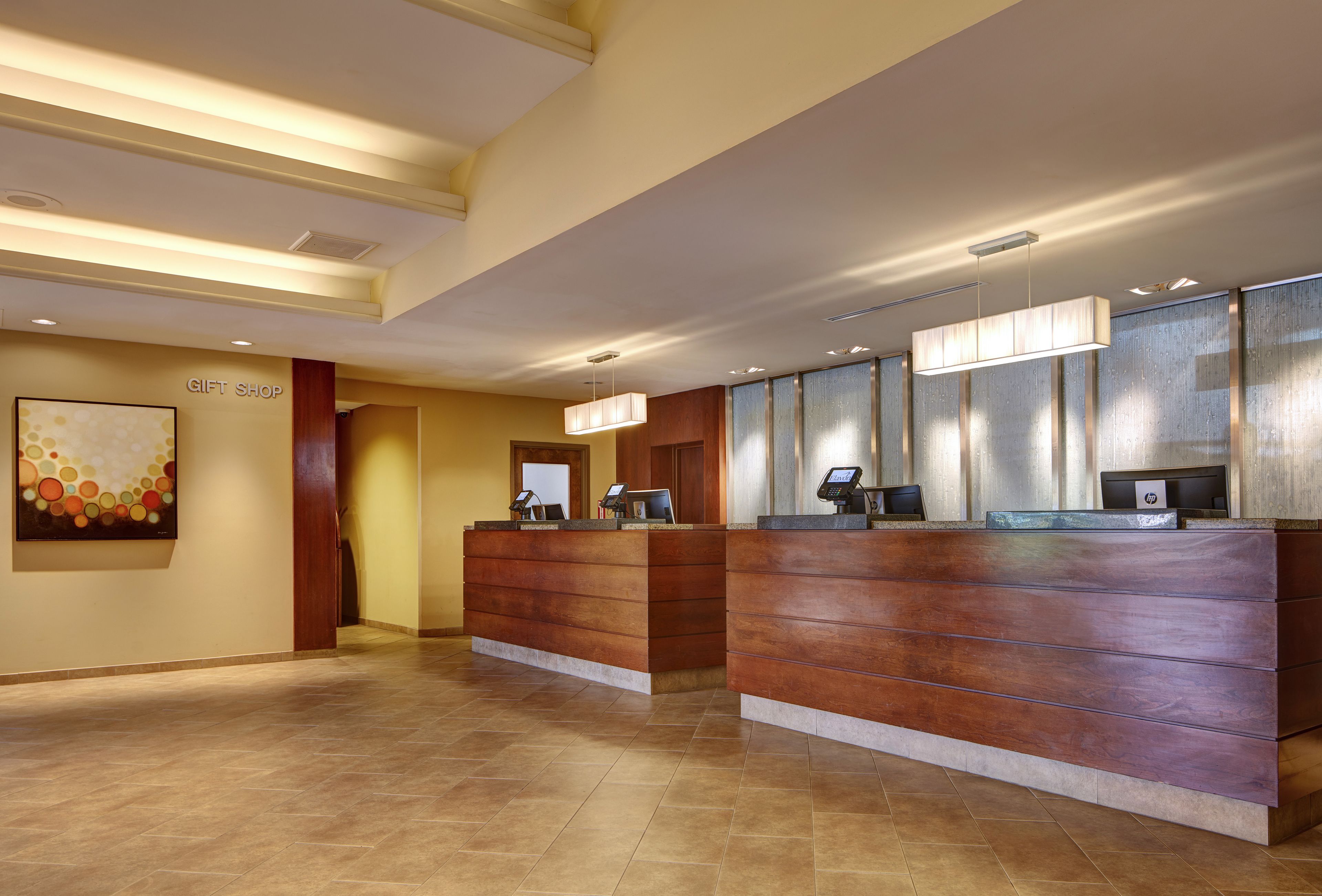 A hotel reception area with a wooden reception desk, a wall-mounted artwork, and a 'Gift Shop' sign.
