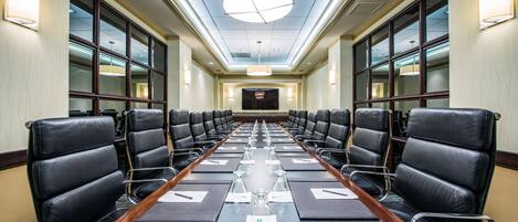 A conference room with rows of black leather chairs, a long table with nameplates, and a large screen at the front.