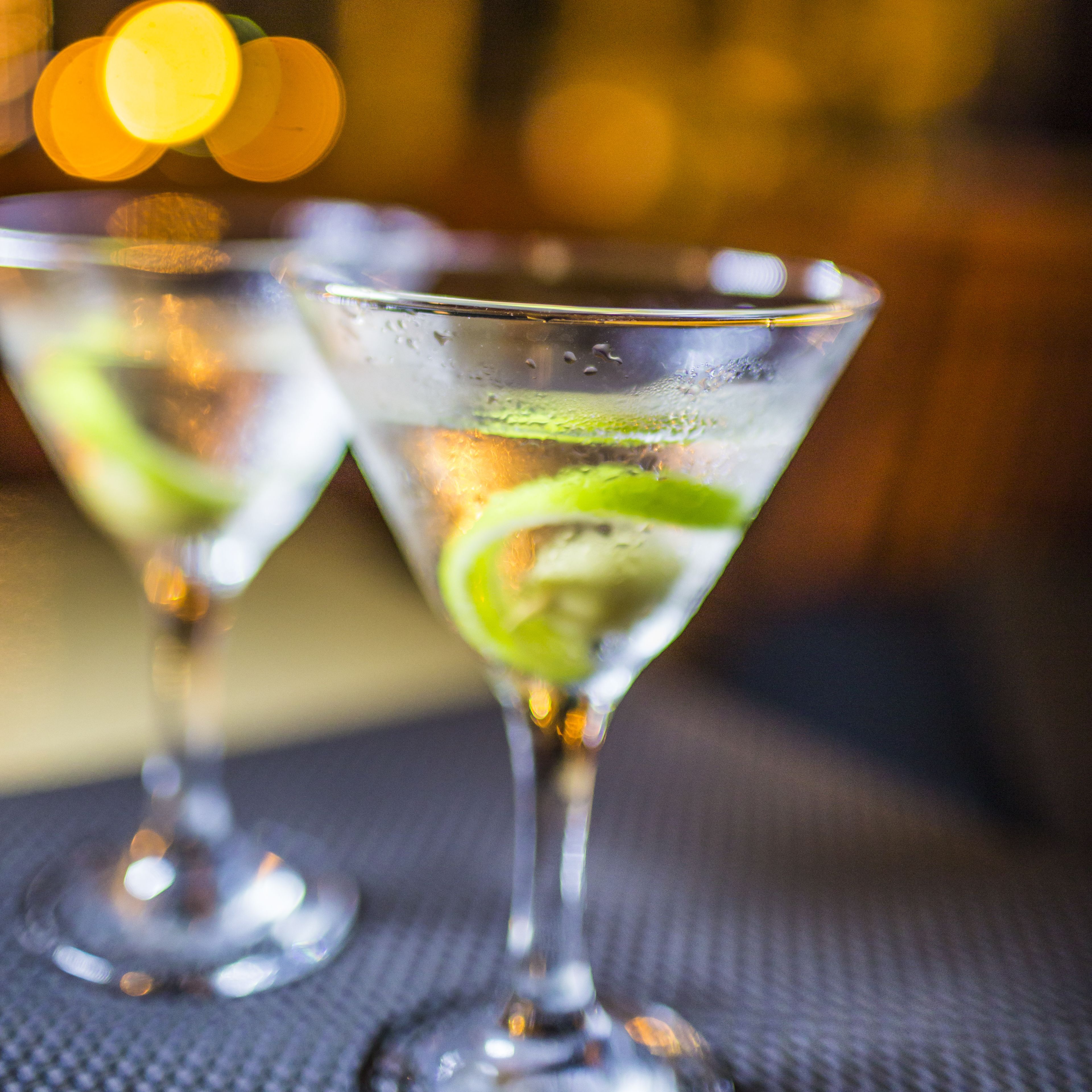 Two martini glasses with lime garnishes on a textured surface.