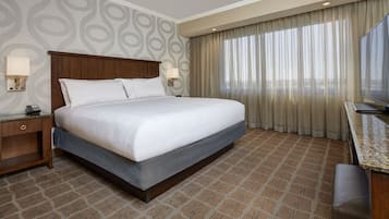 Una habitación de hotel con una cama grande, un escritorio con televisor y una alfombra estampada.