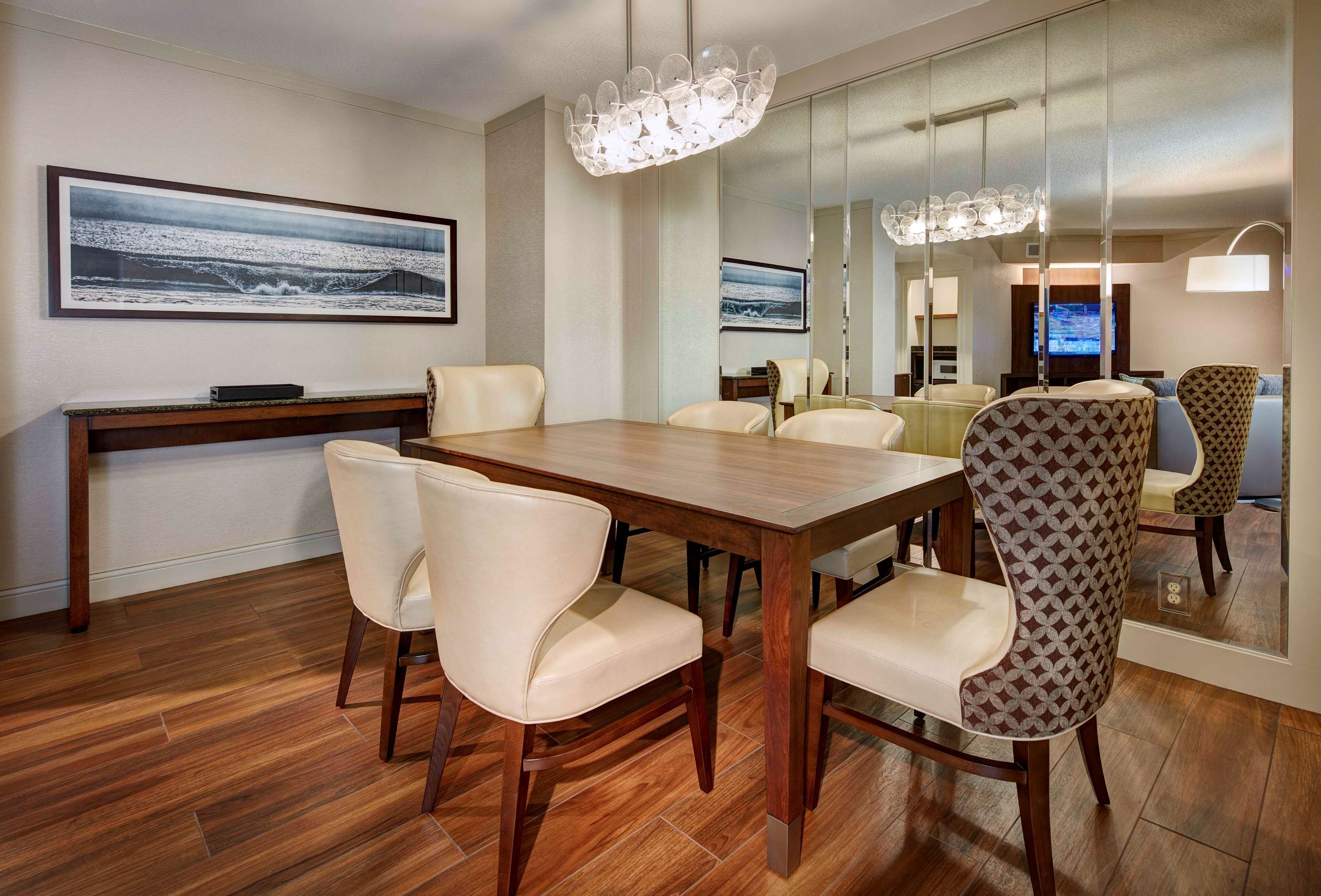 A modern dining area with a wooden table, leather chairs, and a chandelier.