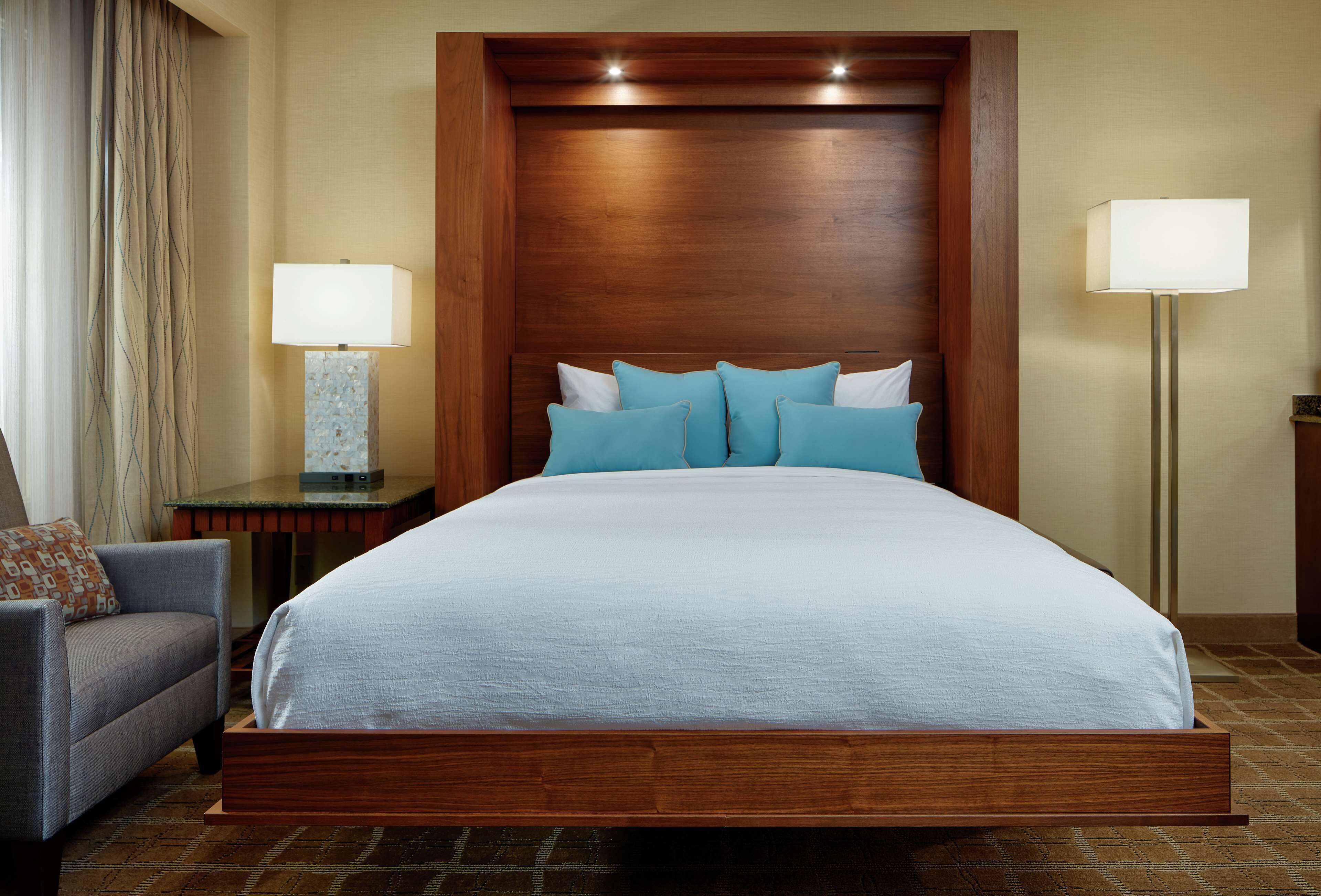 A hotel room with a large bed, two bedside lamps, a chair, and a nightstand.