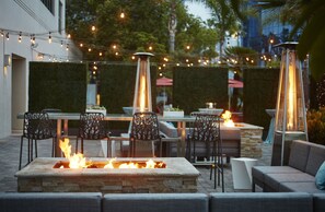 Une terrasse extérieure dotée d’un foyer en pierre, de sièges d’extérieur, de guirlandes lumineuses et d’un chauffage vertical et étroit.