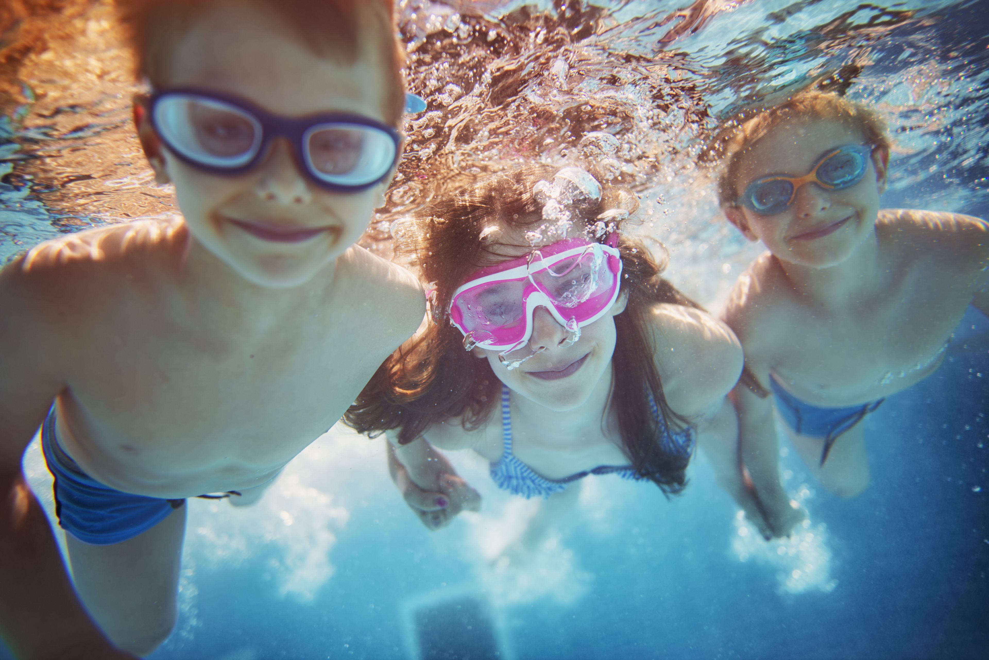 An underwater view of three people wearing goggles, swimming in a pool.