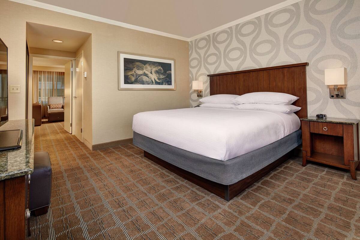 Ein Hotelzimmer mit einem großen Bett, einem Schreibtisch mit Computer, einem Stuhl und einer Wandleuchte.