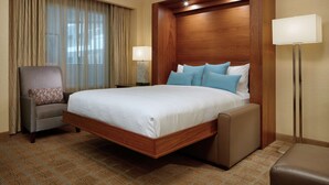 A hotel room with a large bed, a chair, a nightstand, and a lamp.