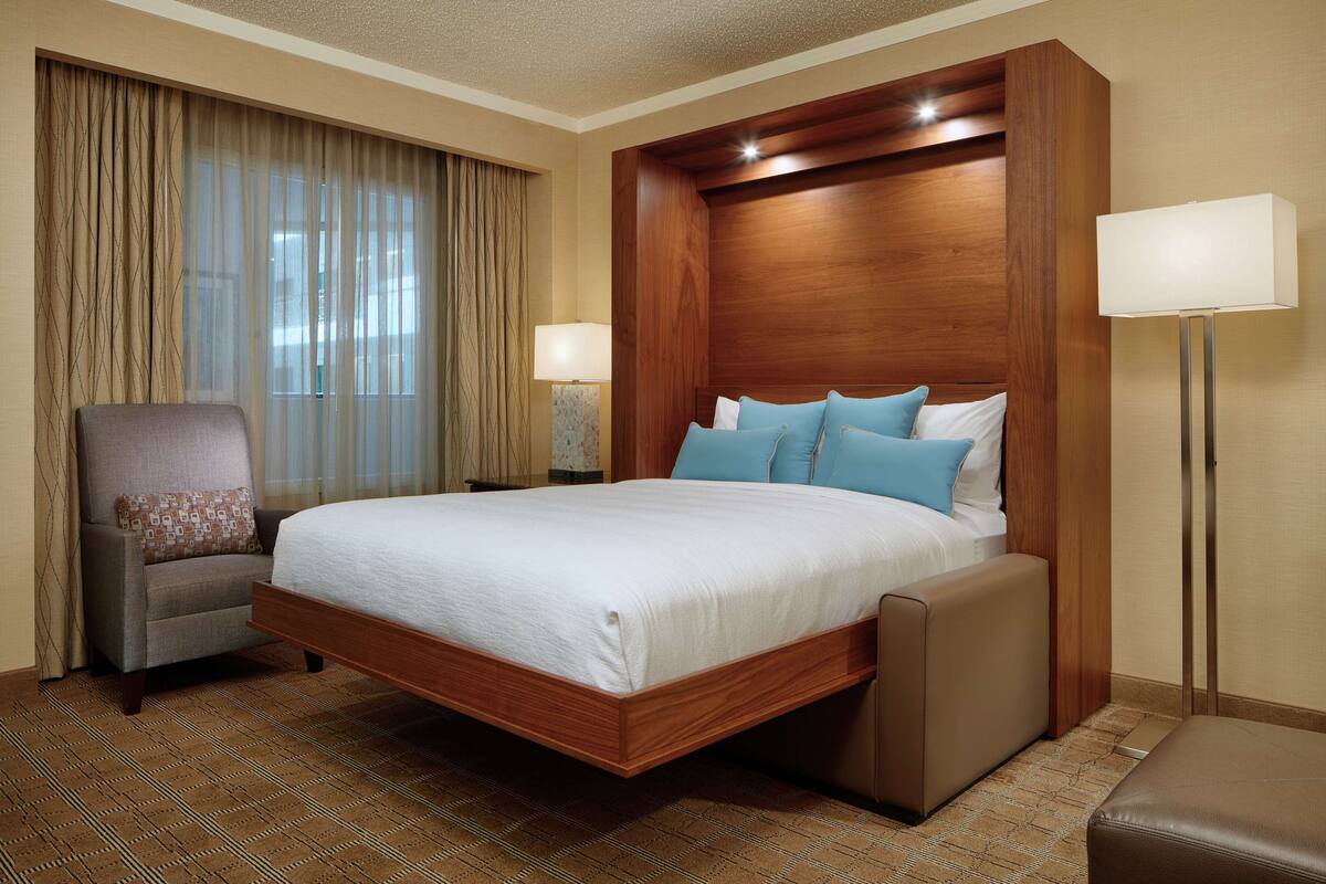 Ein Hotelzimmer mit einem großen Bett, einem Sessel, einem Nachttisch und einer Lampe.