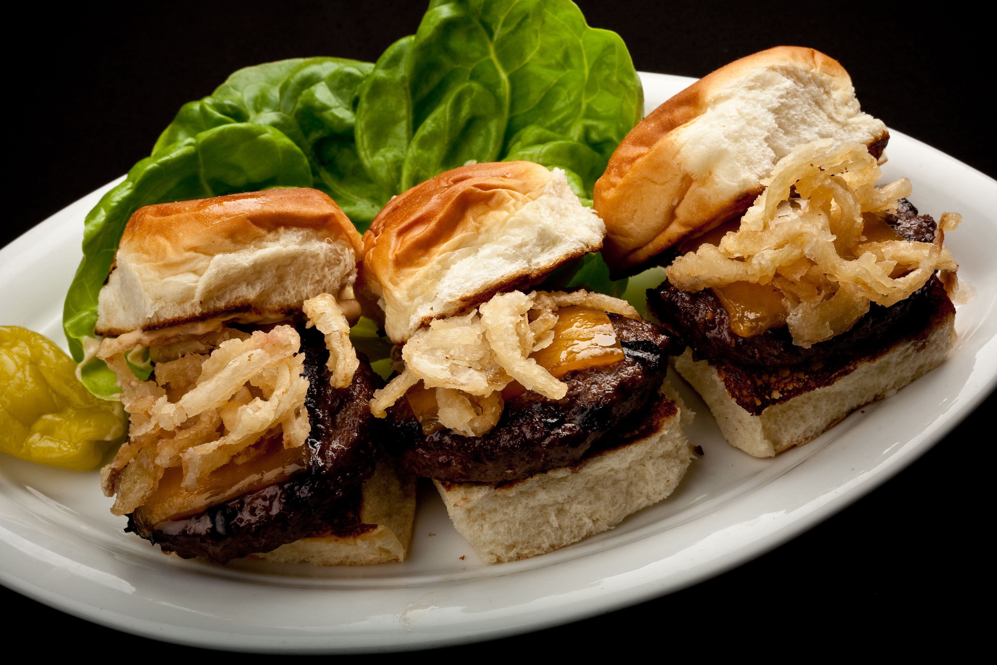 A plate with three burgers, lettuce, and pickles.