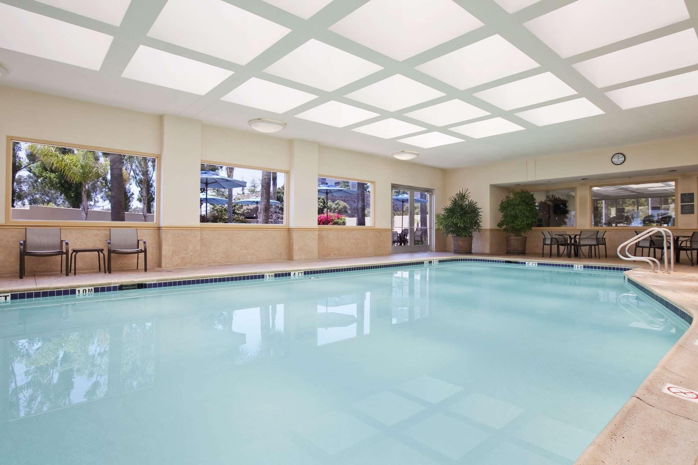 Una piscina con acqua cristallina azzurra, circondata da pareti beige e ampie finestre.