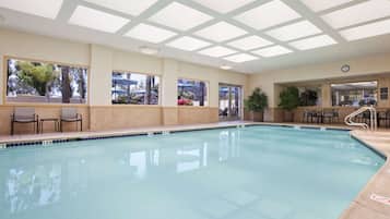 Una piscina con acqua cristallina azzurra, circondata da pareti beige e ampie finestre.
