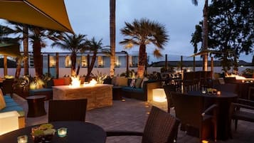 Relax and socialize in this inviting patio area with a fire pit, comfortable seating, and a dining table surrounded by palm trees.