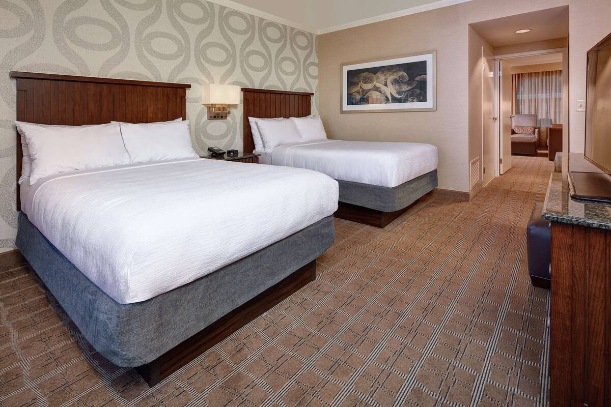 Ein Hotelzimmer mit zwei Betten, einem Holz-Kopfteil, einem Bild an der Wand und einem gemusterten Teppich.