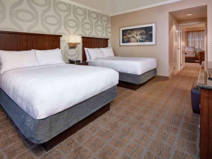 Habitación de hotel con dos camas, cabecera de madera, un cuadro en la pared y alfombra estampada.
