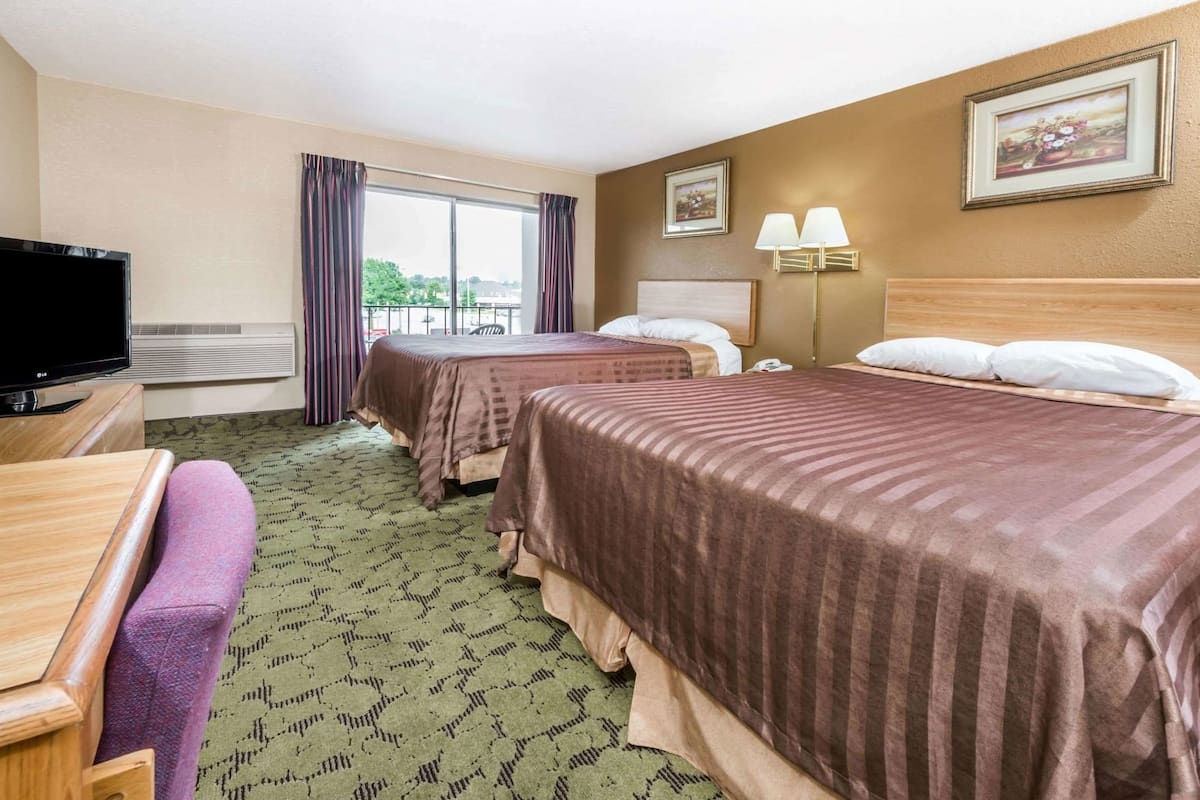 A hotel room with two beds, a TV, a desk, and a window with curtains.