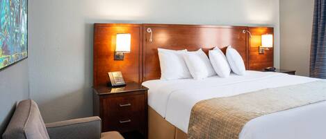 Een hotelkamer met een groot bed, twee nachtkastjes met lampen, een stoel en een schilderij aan de muur.