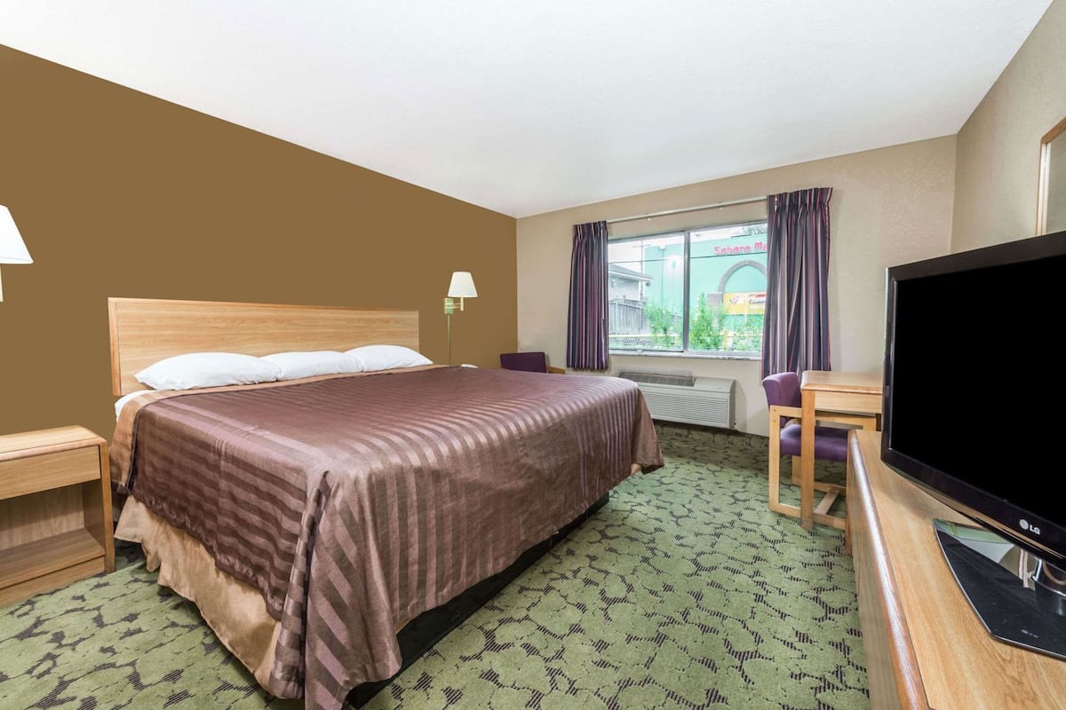 A hotel room with a bed, a desk, a television, and a window with curtains.