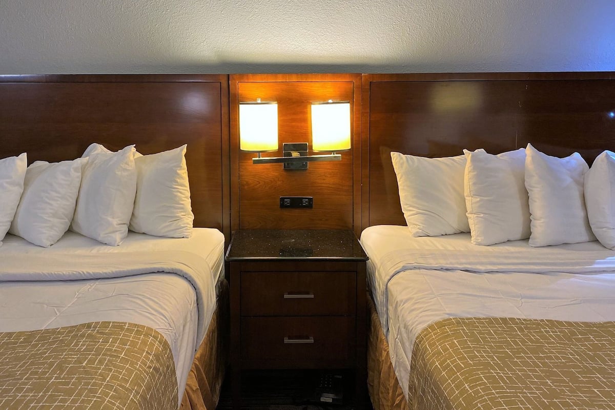 A hotel room with two beds, a nightstand, a wooden headboard, and a wall-mounted light fixture.