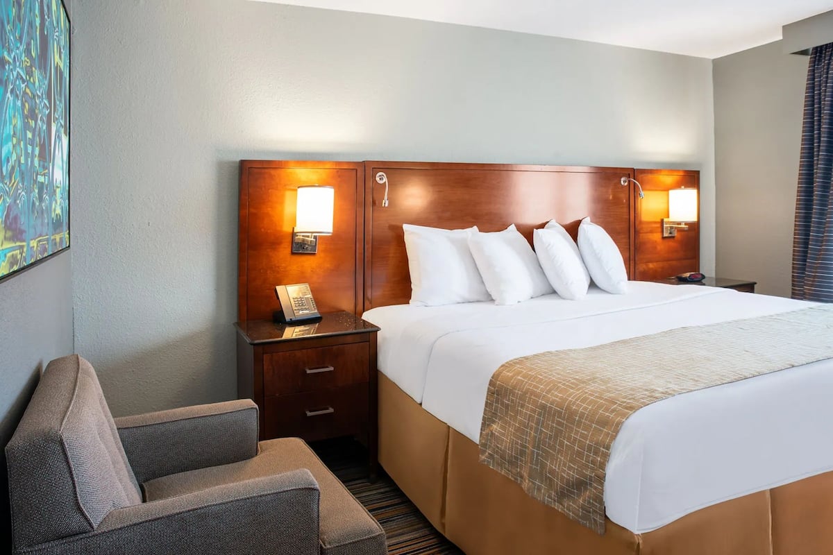 A hotel room with a large bed, two bedside tables with lamps, a chair, and a painting on the wall.