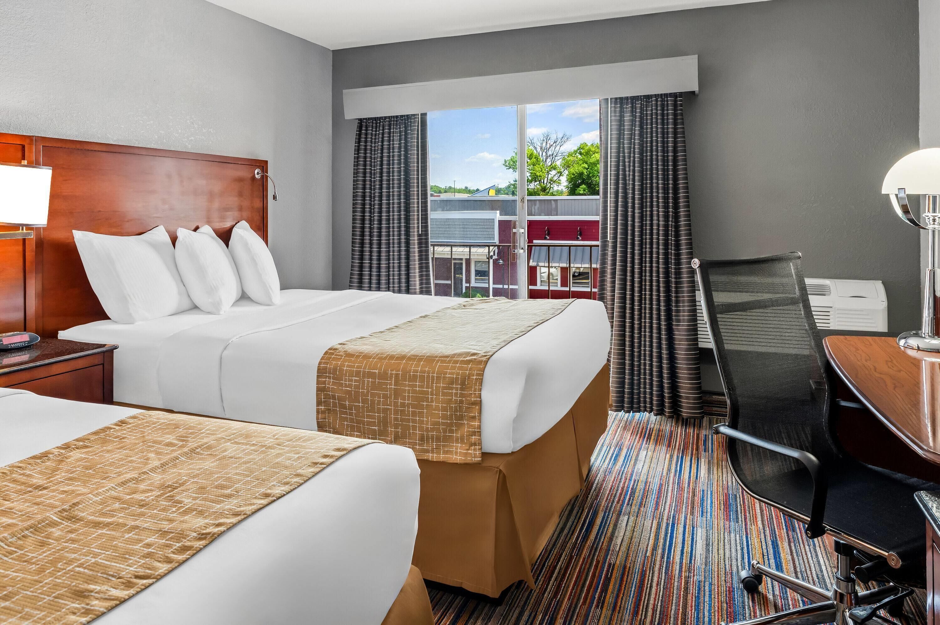 A hotel room with two beds, a desk, and a chair.