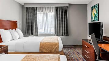 A hotel room with two beds, a TV, a desk, and a window with curtains.