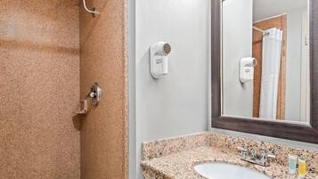 A bathroom with a granite countertop sink, a mirror, and two wall-mounted hair dryers.