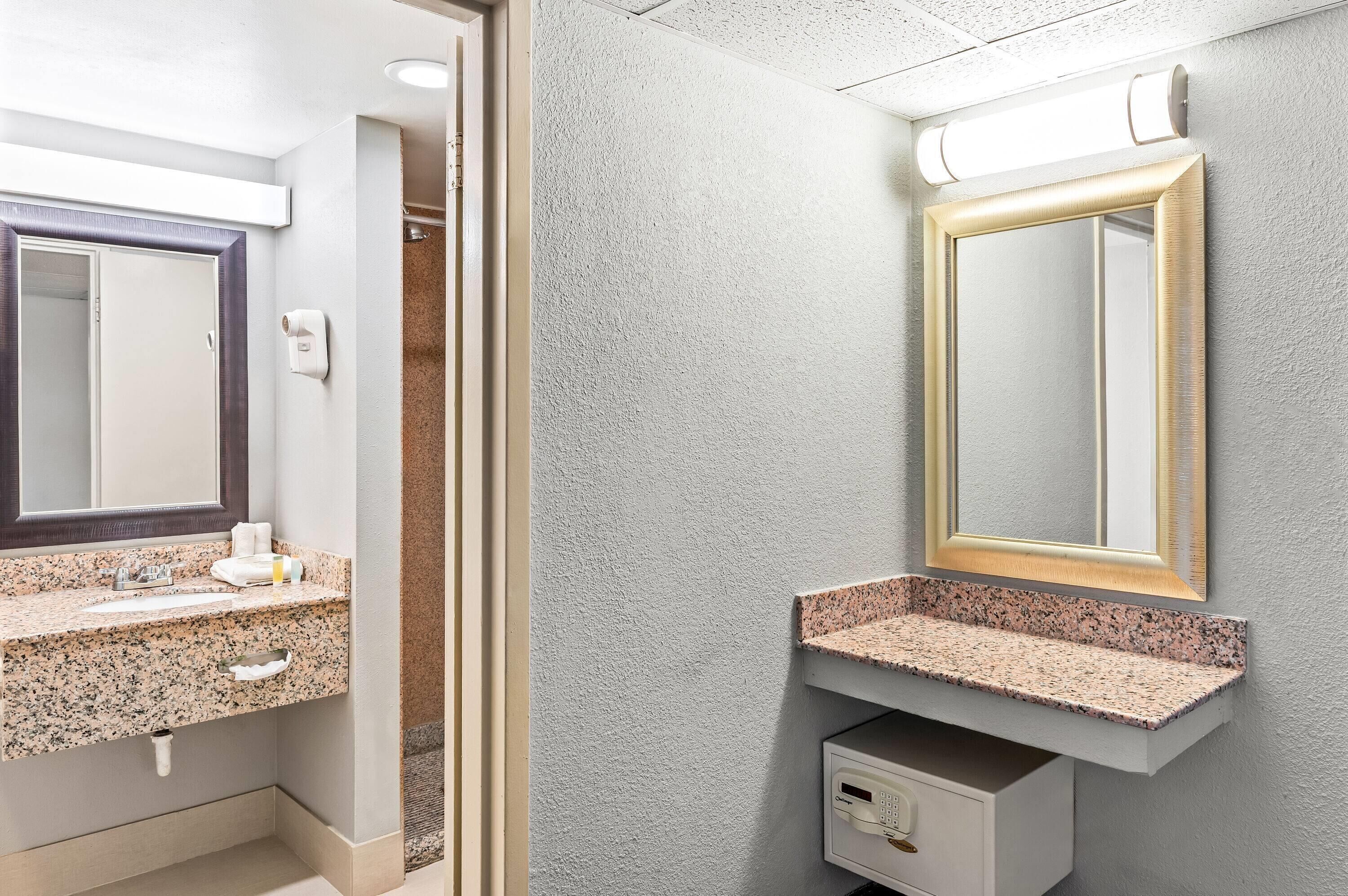 A bathroom with a granite countertop sink, a mirror, and a towel dispenser.