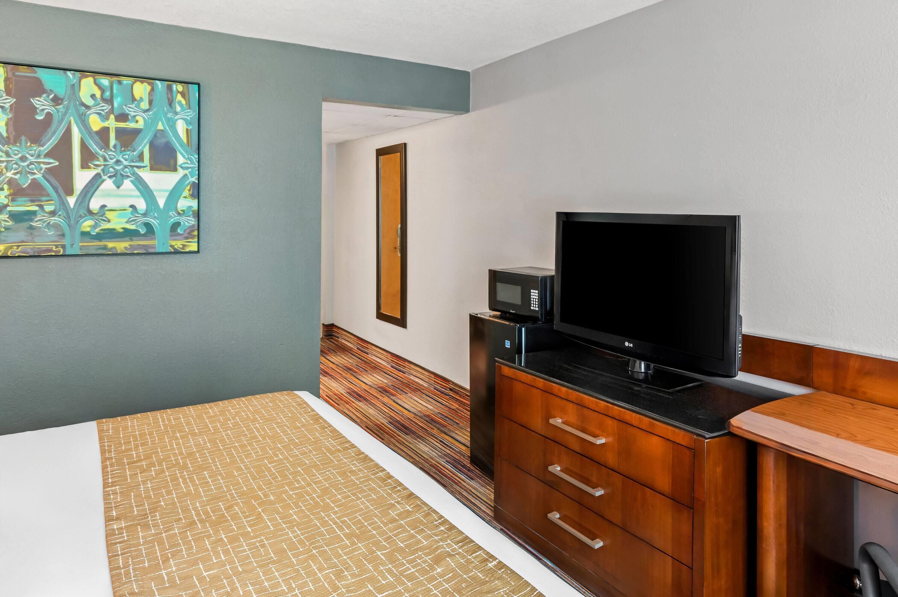 Une chambre d’hôtel équipée d’un lit, d’une commode en bois, d’une télévision et d’un four à micro-ondes.