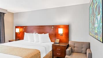 Una habitación de hotel con una cama grande, dos mesitas de noche con lámparas, una silla y un cuadro en la pared.